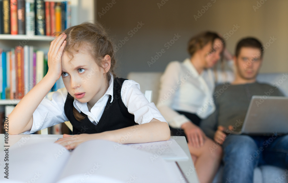 Fototapeta premium Tired little girl doing homework, while her parents resting on the sofa.