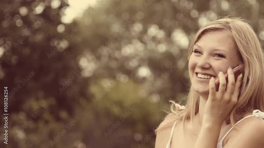 Beautiful young girl having cheerful conversation on cell phone outside. Close up portrait of beauty face of laughing girl talking phone at green trees background. Slow motion video footage. Beautiful young girl having cheerful conversation on cell phone outside. Close up portrait of beauty face of laughing girl talking phone at green trees background. Slow motion video footage.
