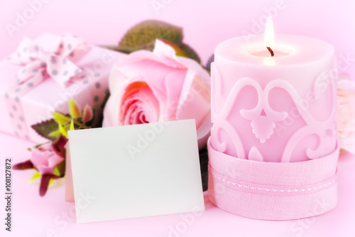 Beautiful festive setting - for Birthday, Engagement, St. Valentine's day occasion - with a greeting card, lit candle, roses and a gift against pastel pink background. With copy space for your text