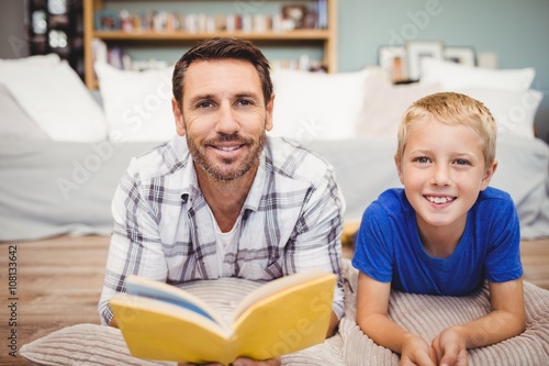 Father and son holding book lying on floor at home