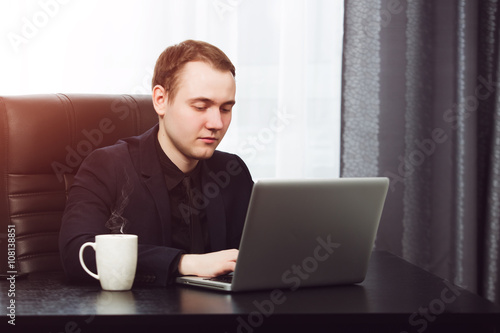 Young business man working on laptop. Hot coffee near