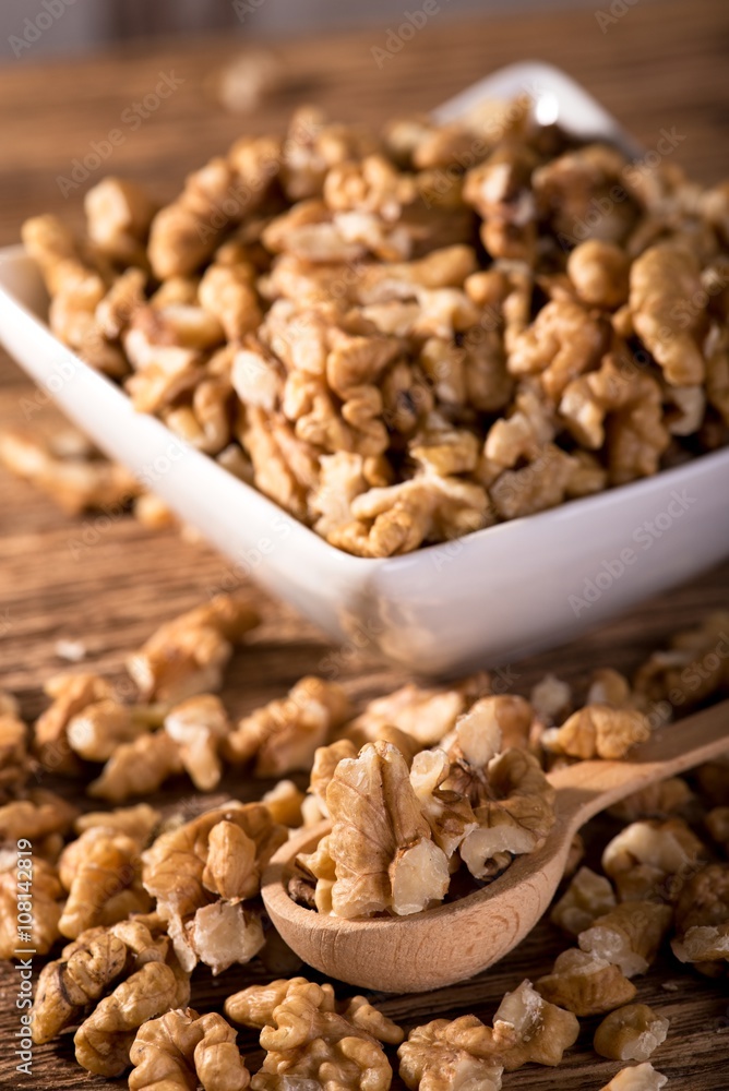 Heap of walnuts in font of white bowl on wooden spoon Heap of walnuts in font of white bowl on wooden spoon