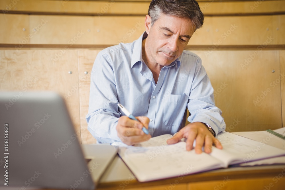 Professor writing in book at desk Professor writing in book at desk