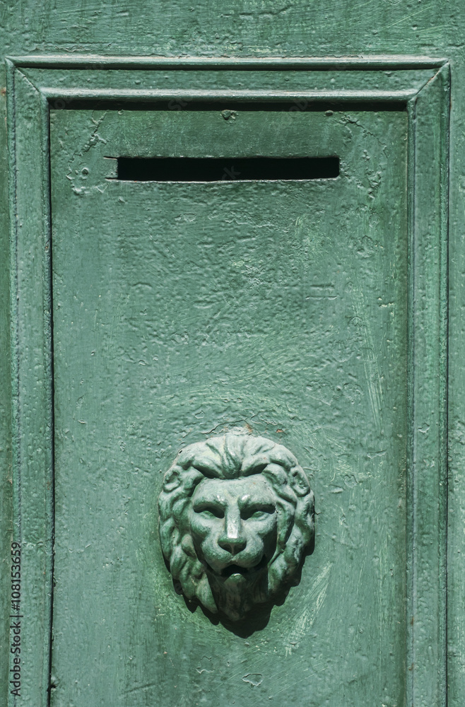 Slit of green metal mailbox with lion's head ornament 