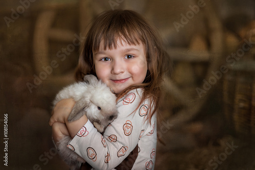 Portrait of cute little girl with white rabbit in hay stack photo