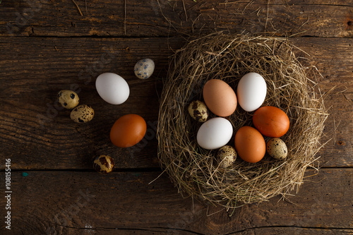 Fresh chicken and quail eggs in a nest on a wooden background