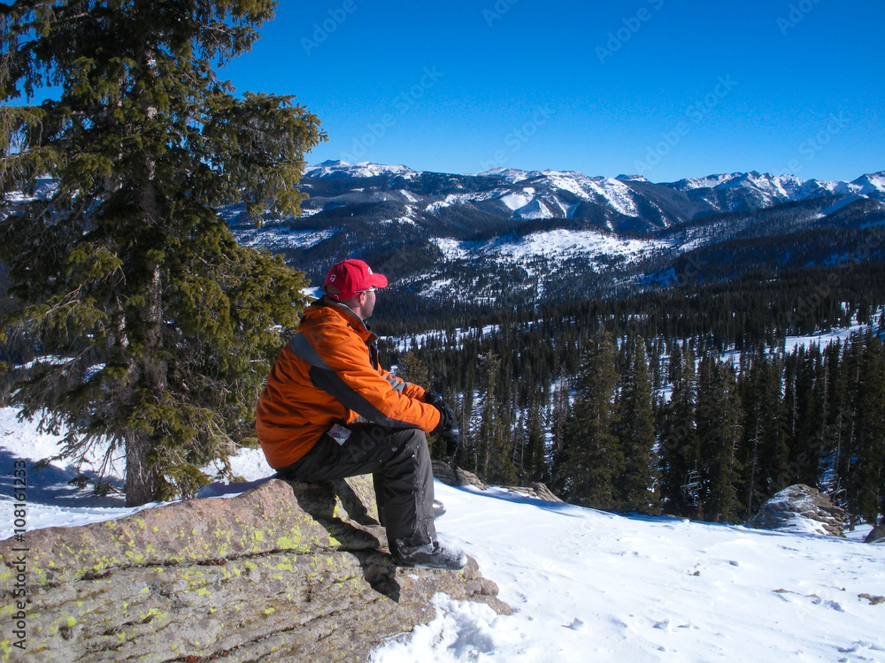 Man sitting in snow looking at mountains.