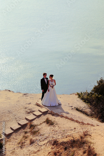 fashion outdoor photo of beautiful couple. gorgeous bride in wedding dress posing with elegant groom on sea cost  