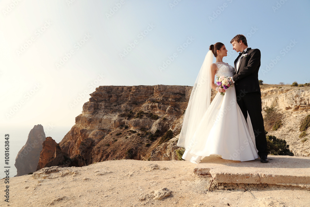 fashion outdoor photo of beautiful couple. gorgeous bride in wedding dress posing with elegant groom on sea cost fashion outdoor photo of beautiful couple. gorgeous bride in wedding dress posing with elegant groom on sea cost