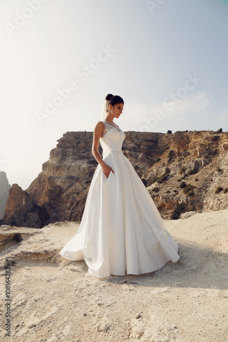 fashion outdoor photo of gorgeous bride in wedding dress posing on sea cost 