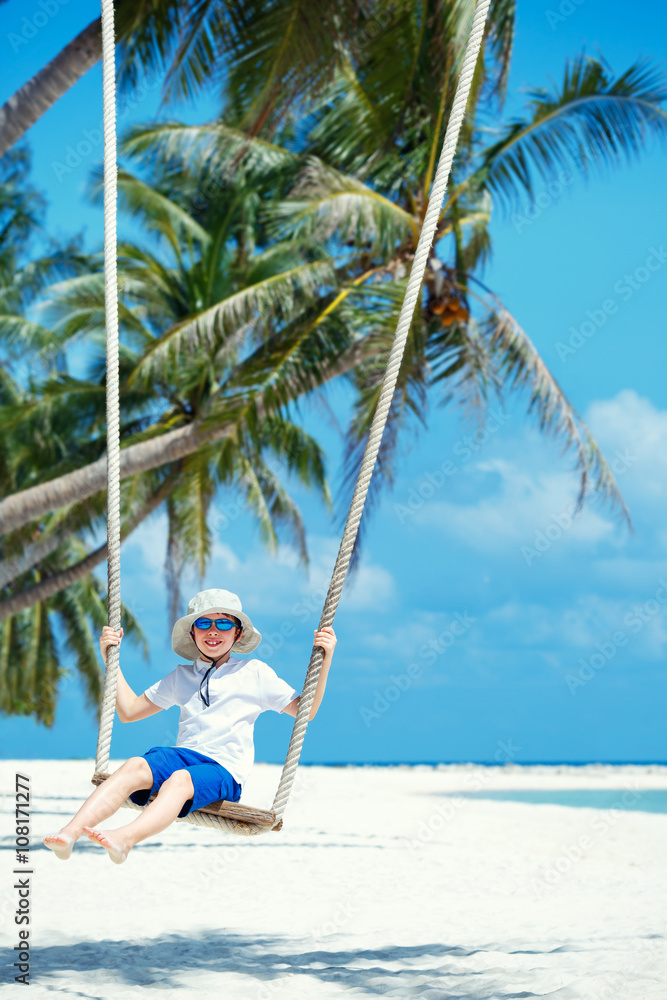 Cute boy having fun swinging at tropical island beach Cute boy having fun swinging at tropical island beach