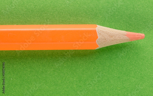 Orange pencil on green background closeup