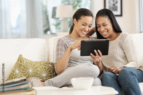 Mother and daughter using digital tablet on sofa photo
