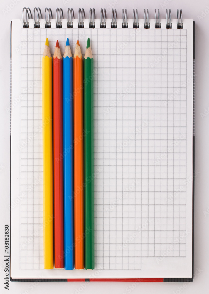 notebook and colored pencils on a white background notebook and colored pencils on a white background