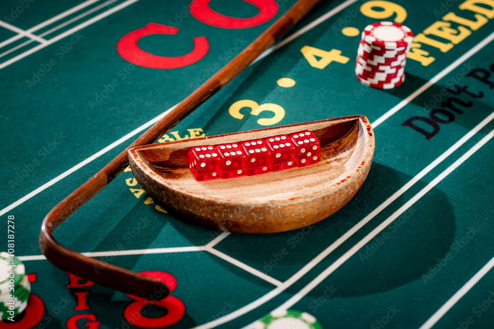 Fototapeta premium Full set of 5 dice in a wooden bowl next to the stick on a craps table with stacks of casino chip around