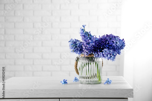 Beautiful hyacinth flowers in glass vase against brick wall background