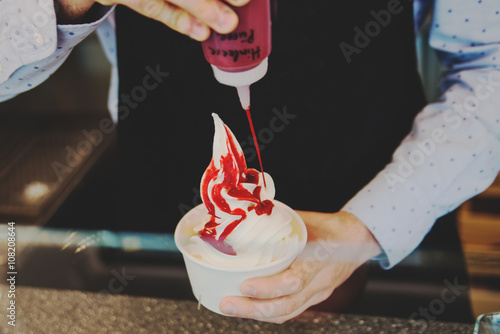 seller pours sauce on a soft frozen yogurt in white take away cup photo