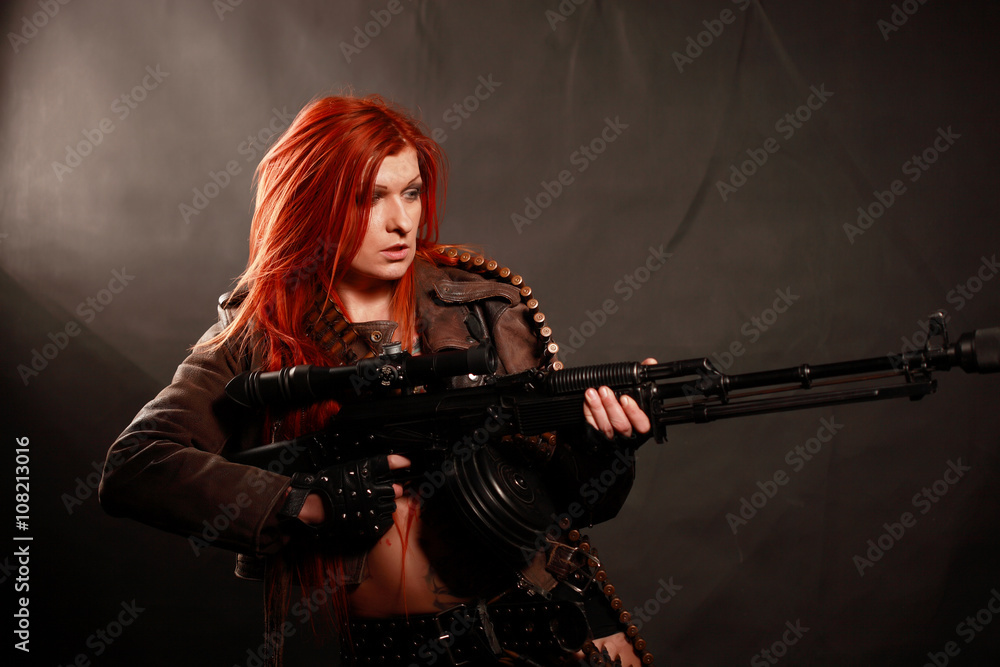 Studio shot of attractive redhead punk girl with rifle and sniper equipment, taken againstwall covered with dark fabric Studio shot of attractive redhead punk girl with rifle and sniper equipment, taken againstwall covered with dark fabric