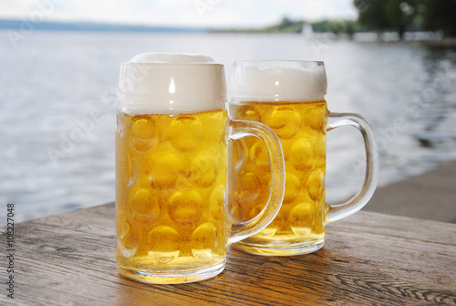 Kühles, frische Bier / Zwei Bierkrüge mit frischem Bier draußen am See  