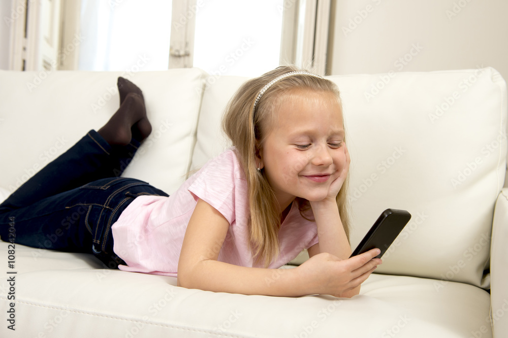 happy blond little girl on home sofa using internet app on mobile phone happy blond little girl on home sofa using internet app on mobile phone
