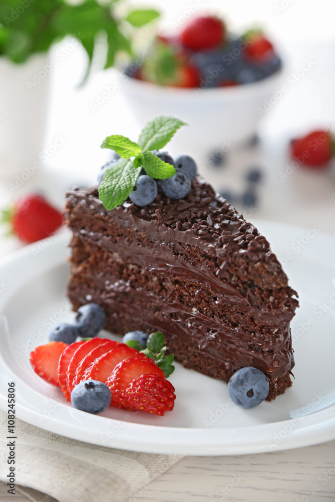 Chocolate cake with chocolate cream and fresh berries on plate, on light background Chocolate cake with chocolate cream and fresh berries on plate, on light background