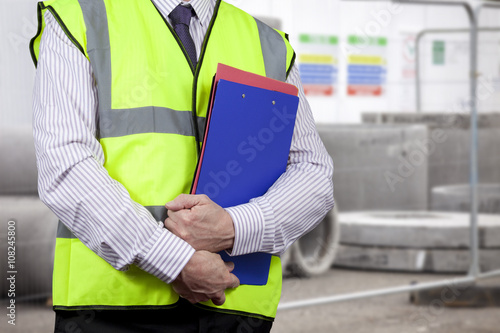 Building surveyor in high visibility carrying clipboard on site