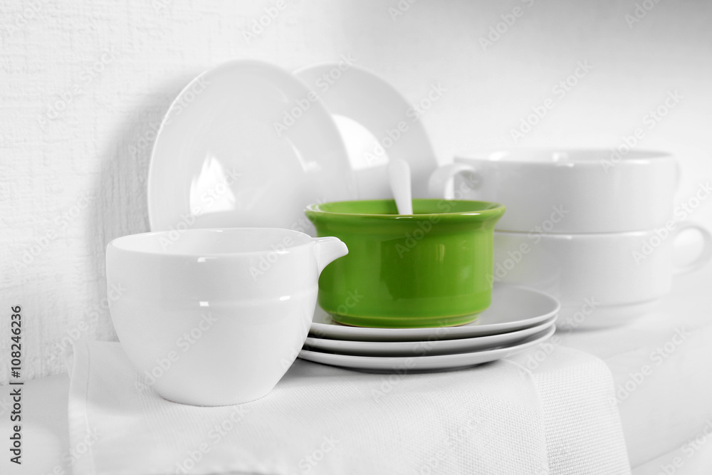 Set of tableware with napkin on shelf against white wall background Set of tableware with napkin on shelf against white wall background