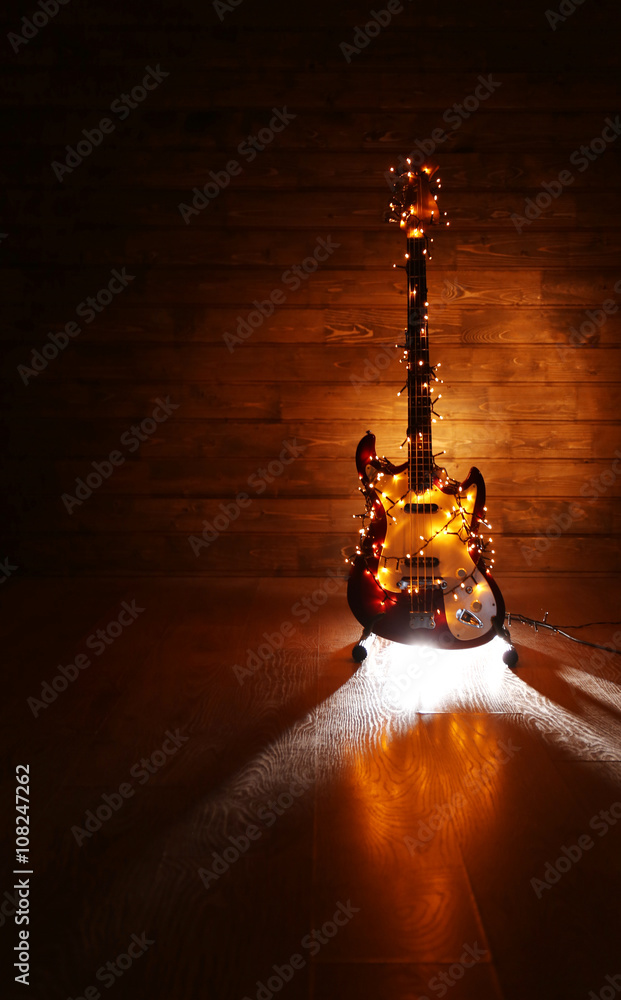 Fototapeta premium Electric guitar with lighted garland on dark wooden background