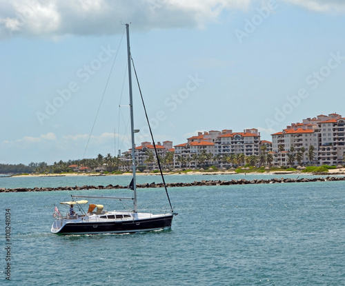 Sail boat on government cut inlet with luxury fisher island conds in the background.