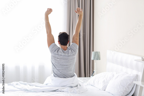 Wallpaper Mural A young man waking up in bed and stretching his arms Torontodigital.ca