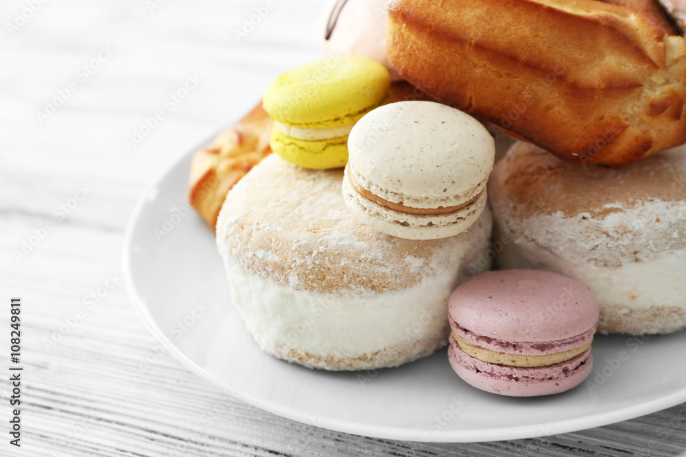 Plate of cakes and macaroons on wooden background, closeup