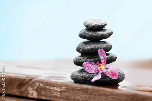 Stack of spa stones with pink orchid on wooden wet bridge