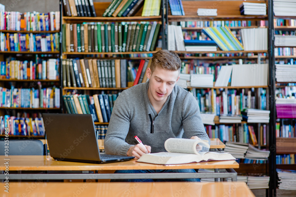 Male student with laptop studying in the university library Male student with laptop studying in the university library
