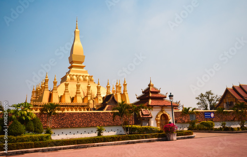 Golden buddhist pagoda of Phra That Luang Temple under blue sky.
