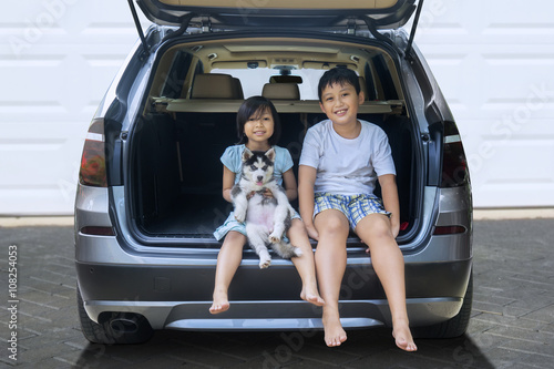 Happy children sit in the car with husky dog