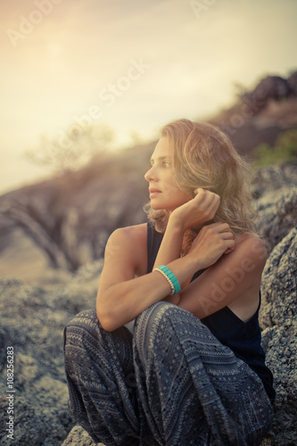 beautiful young woman sitting on the rocks at sunset background © olezzo