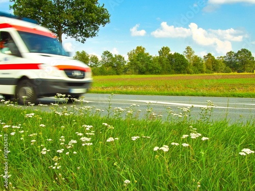 Krankenwagen fährt im Notfall schnell über Landstraße, Landschaft im Hintergrund, Niedersachsen, Deutschland