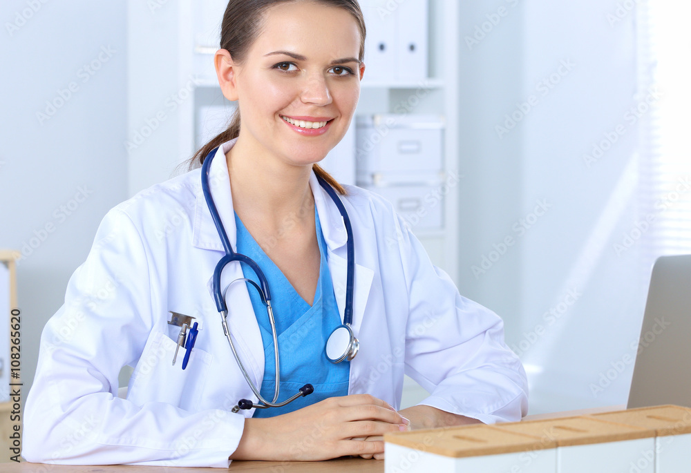Beautiful young smiling female doctor sitting at the desk and writing. Beautiful young smiling female doctor sitting at the desk and writing.