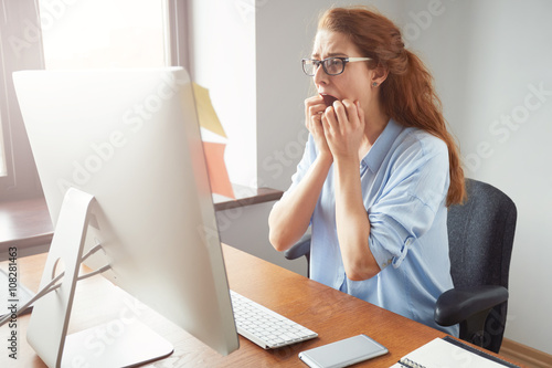 Stressed shocked businesswoman sitting at the table in front of computer in the office looking stunned, mouth wide open. Negative human face expressions, emotions, body language reaction