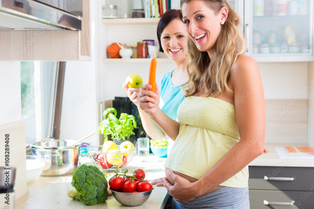 Pregnant woman and girlfriend cooking healthy in kitchen Pregnant woman and girlfriend cooking healthy in kitchen
