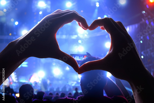 Silhouette of a heart shaped hands and crowd of Audience at live concert, light illuminated is power of music concert