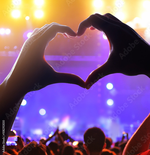 Silhouette of a heart shaped hands and crowd of Audience at live concert, light illuminated is power of music concert