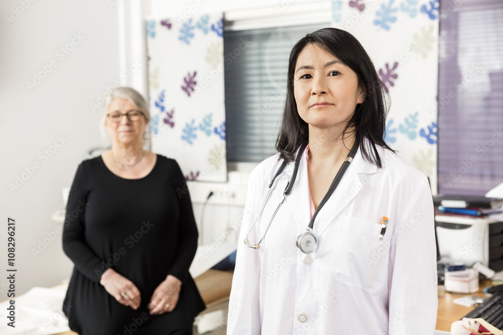 Confident Doctor Standing While Patient Sitting In Background Confident Doctor Standing While Patient Sitting In Background