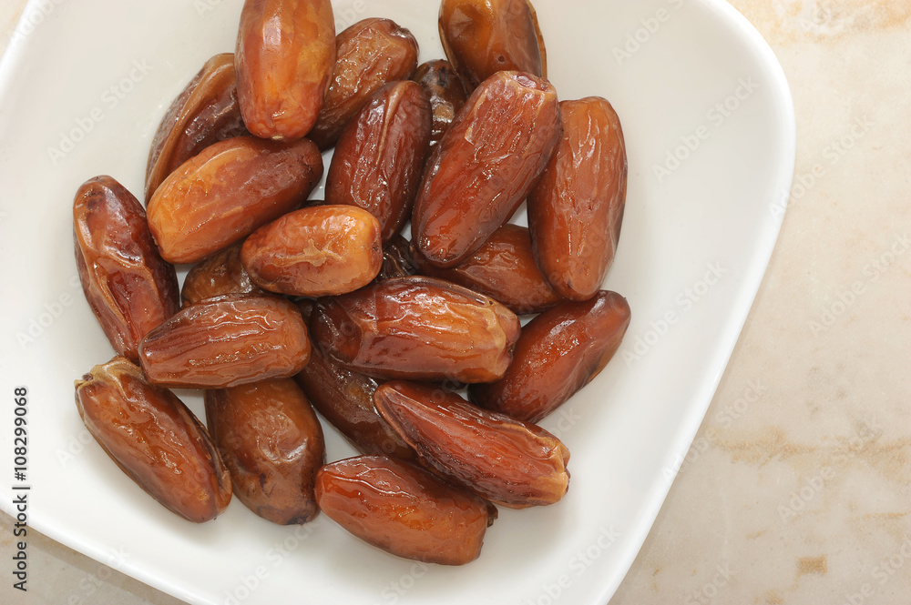 Dried dates fruit in a bowl, on a marble background Dried dates fruit in a bowl, on a marble background