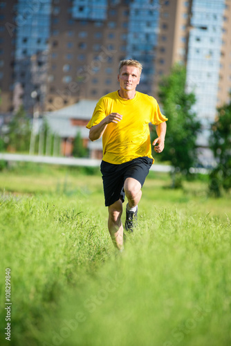 Running man jogging in city street park at beautiful summer day. Sport fitness model caucasian ethnicity training outdoor.