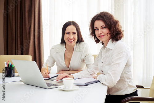 Two young women teamworking with gadgets at the table