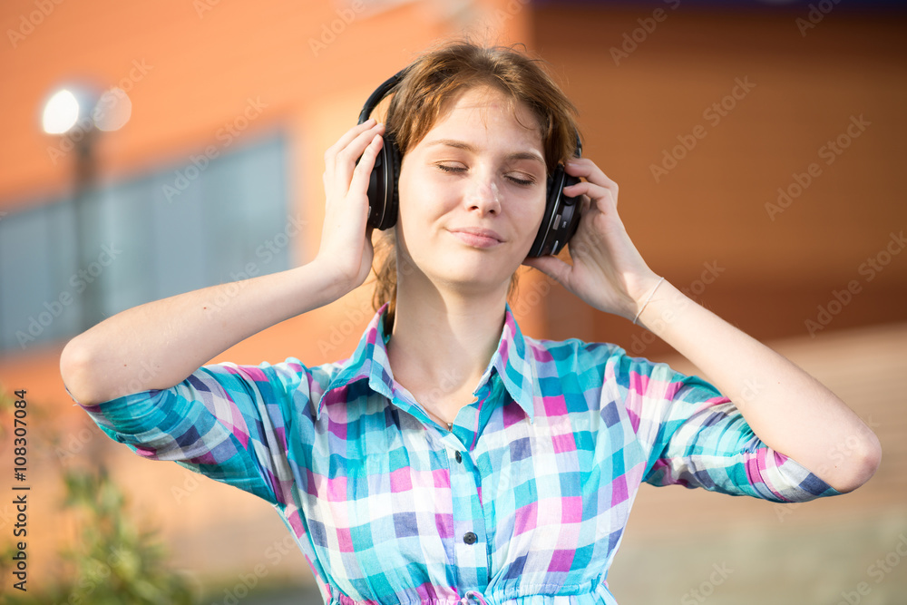 Fototapeta premium Young beautiful girl listening to music player on the street. tudent woman at campus park.