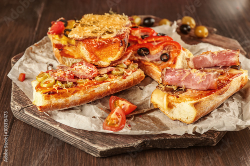 Hot pizza baguettes with bacon, ham, salami and olives on wooden table