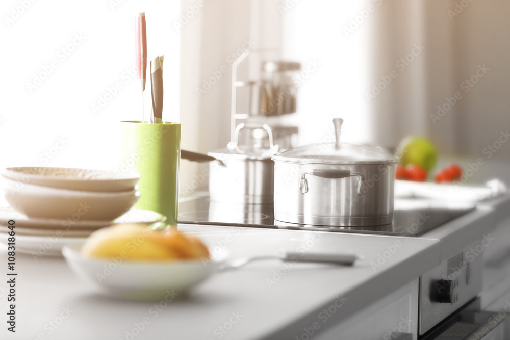Modern table and electric stove with utensils in the kitchen beside window Modern table and electric stove with utensils in the kitchen beside window