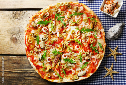 Pizza with seafood, red pepper and green olives on wooden table